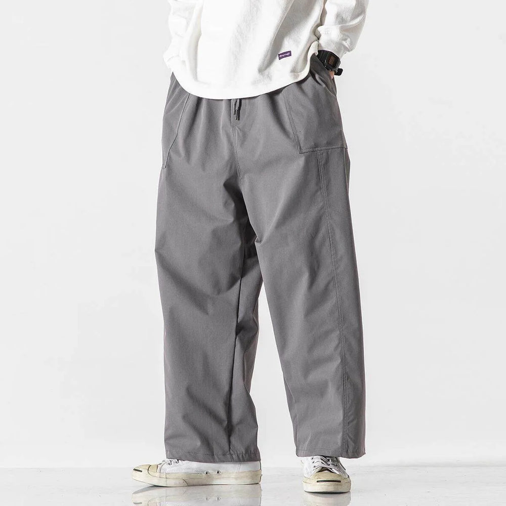 Person wearing gray pants and a white shirt on a plain background